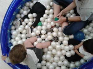 Several children and a teacher enjoy exploring the sensory aspect of having balls in a children's pool.