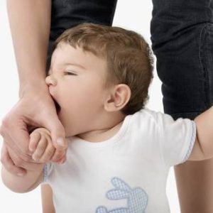 A toddler, being held by their hands by an adult, is biting the adults hand.